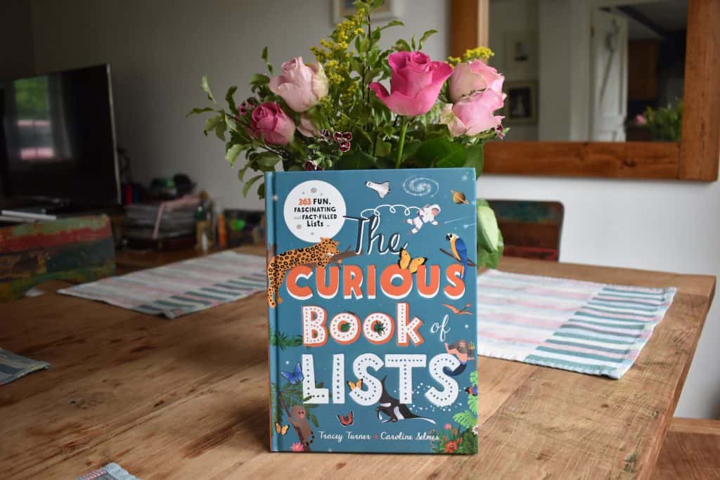 Book 'The Curious Book of Lists' on a table with pink flowers behind it