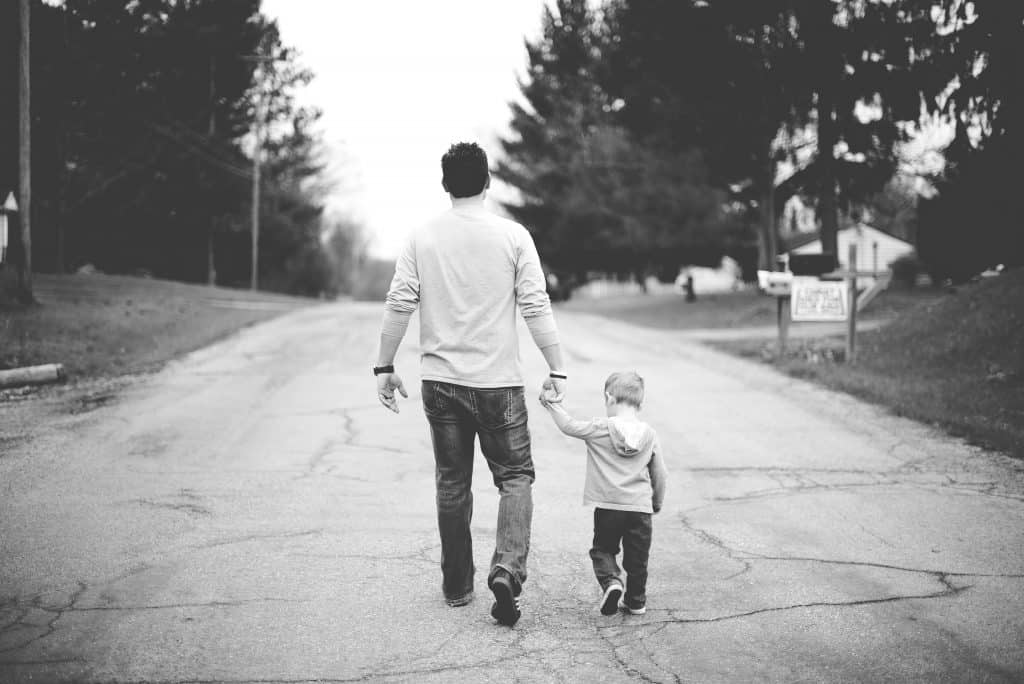 Man and small boy walking down a road (away from the camera)