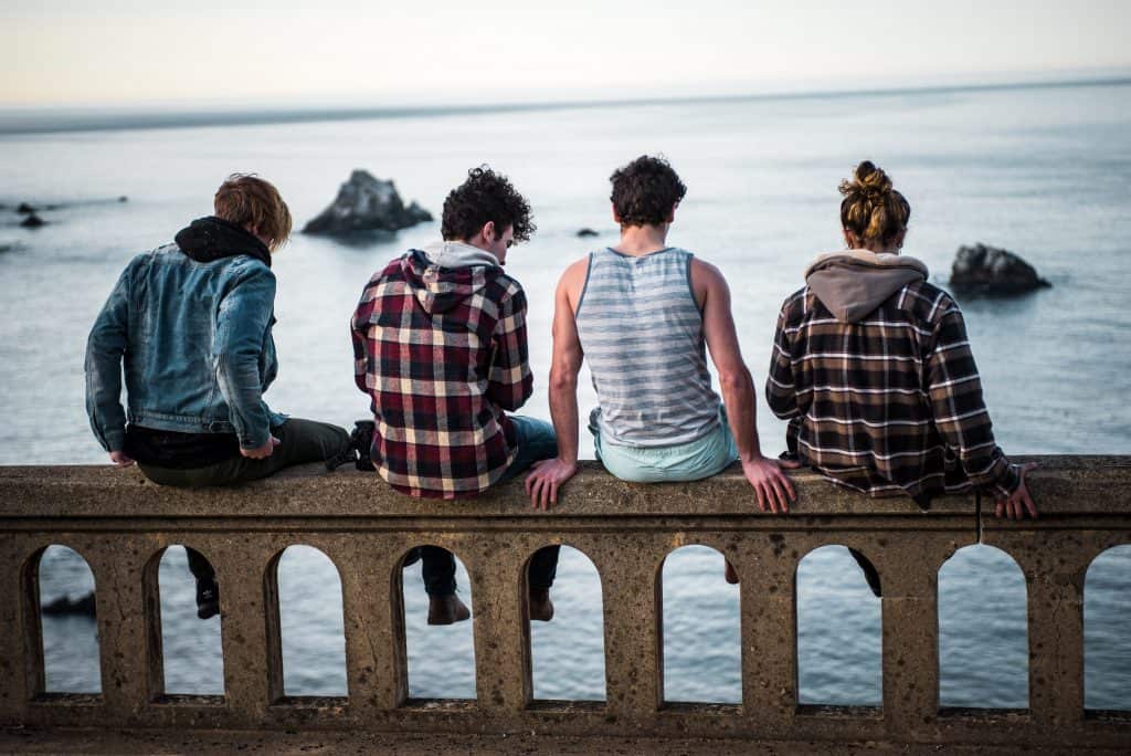 Four teenage boys sitting on a bridge together and looking out to sea