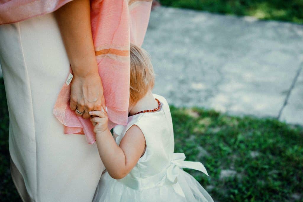 Girl hiding behind her mother's scarf and holding her hand