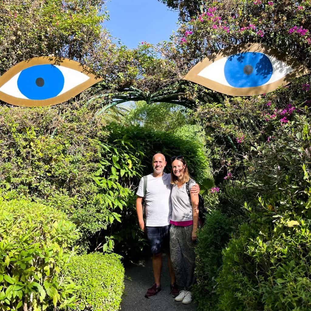 Man and woman standing under an arch in a garden with two large eyes above them