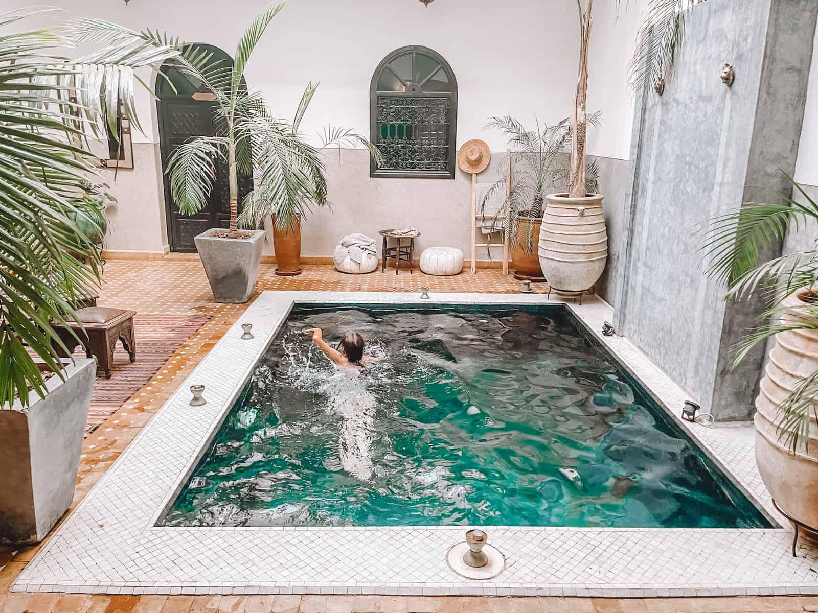 Girl swimming in a small indoor pool in a riad in Morocco with plants surrounding her