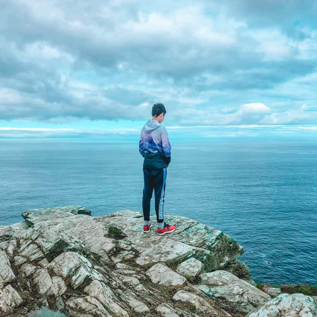Boy standing on rocks looking out to the sea