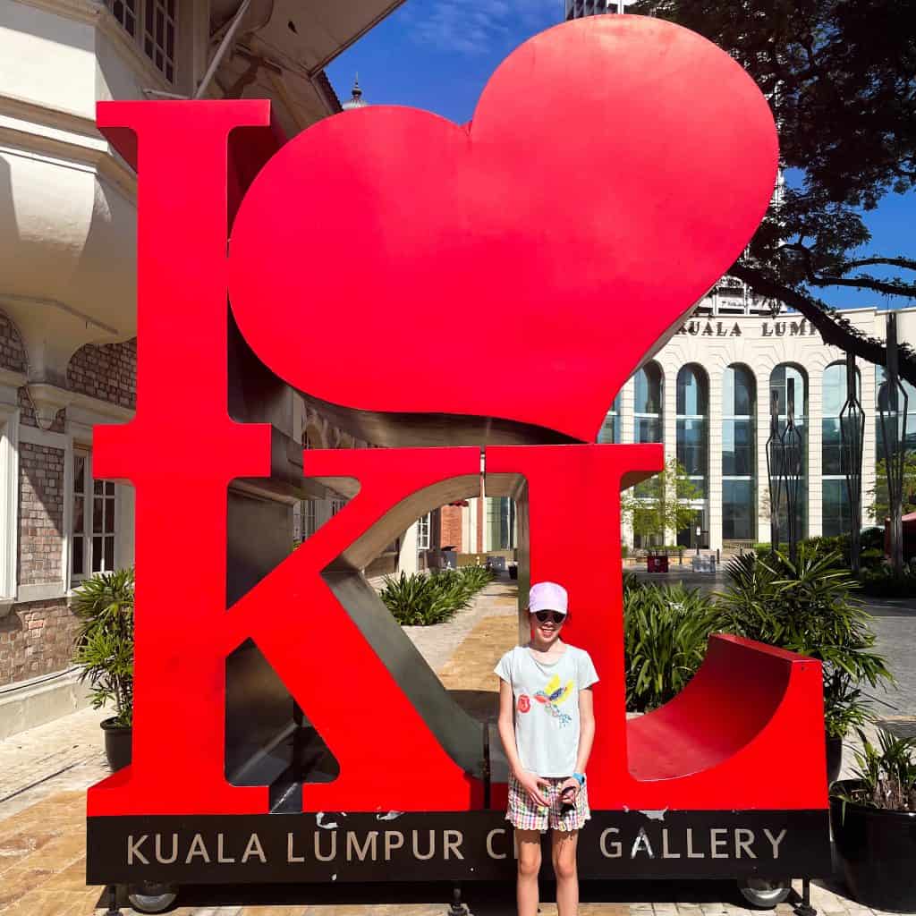Child standing in front of a red 'I heart KL' sign