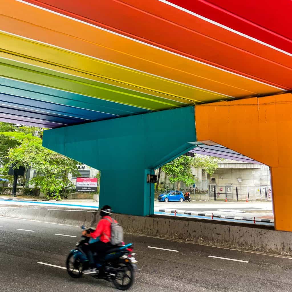 Man on motorbike driving under a colourful bridge