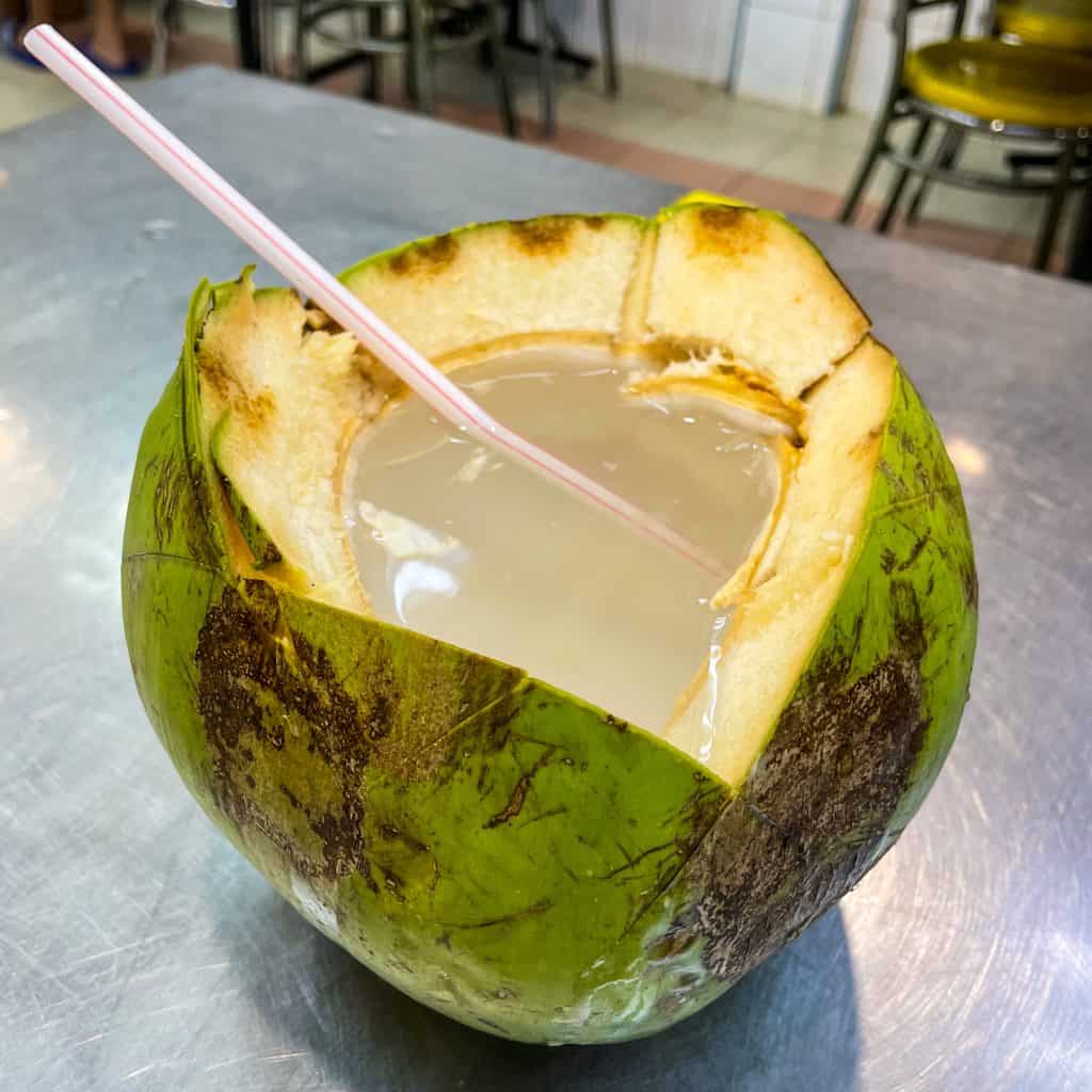 Open coconut with coconut milk and a straw inside