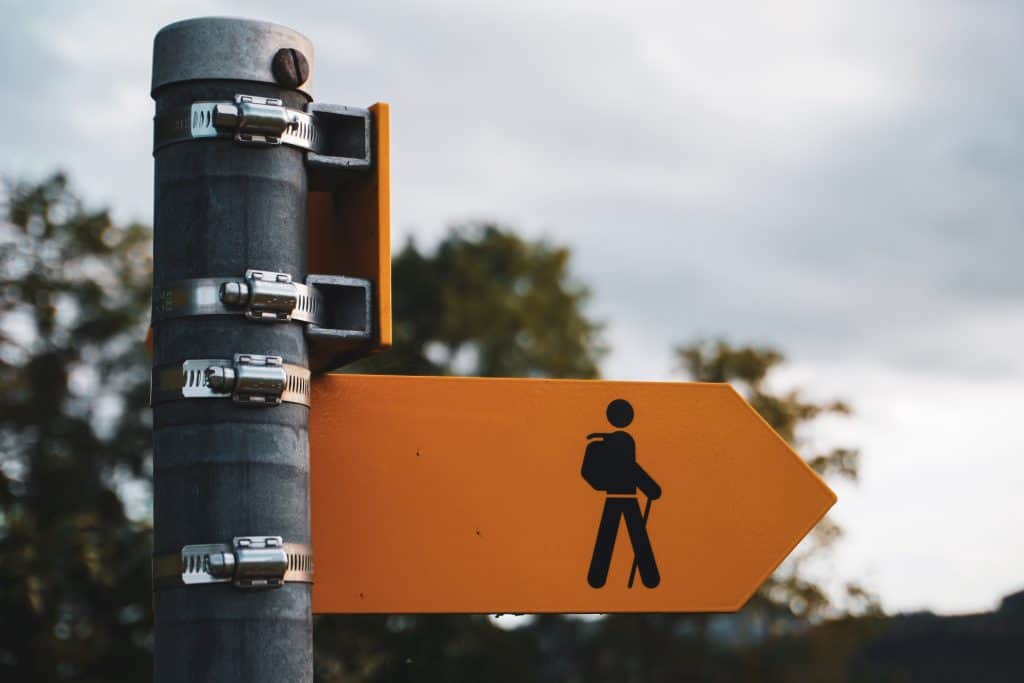 Road sign with yellow pointer with stick figure of a walker on it