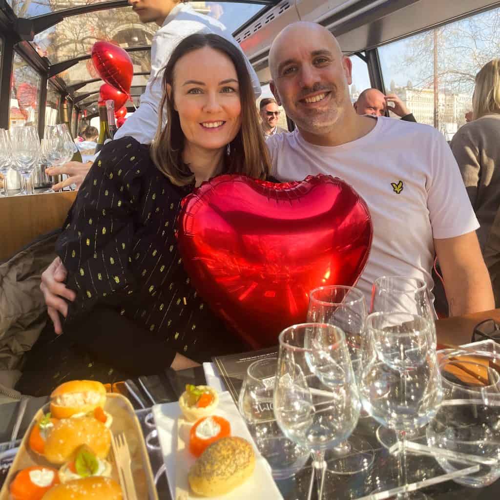 Man and woman holding a red heart balloon and dining on the Bustronome bus in Paris