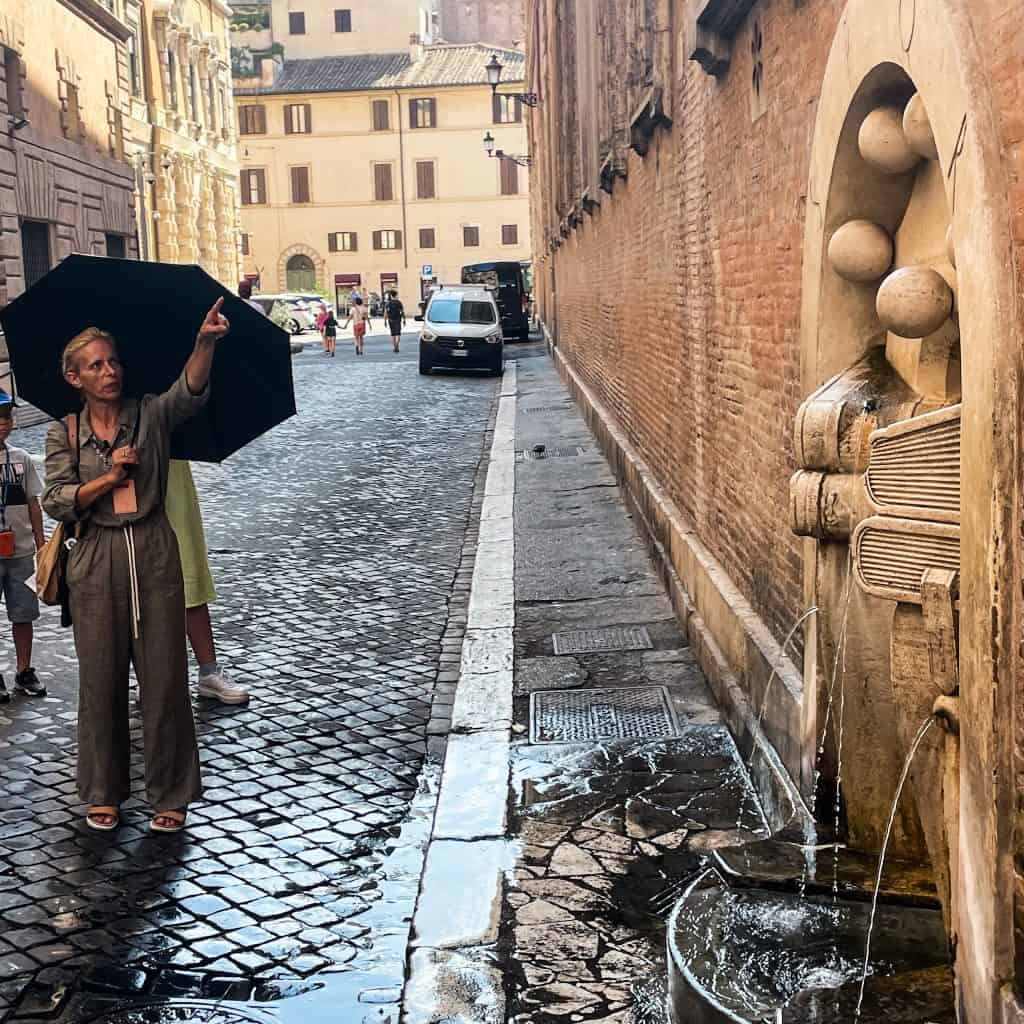 A walking tour in Rome; a woman points at a fountain in a side street