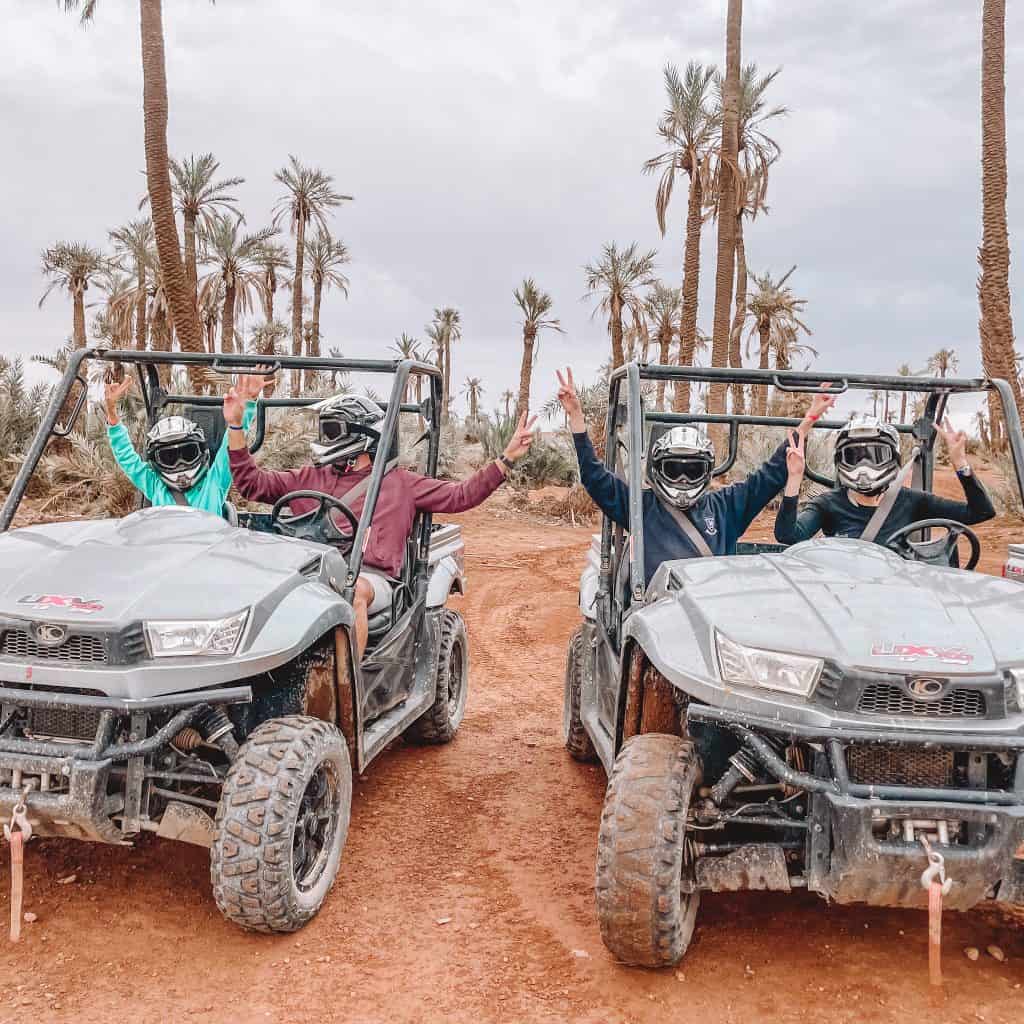 Desert buggies with two people in each one and palm trees behind