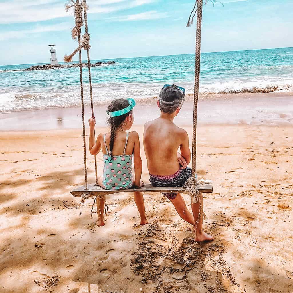 Boy and girl on a swing at a beach looking out to sea