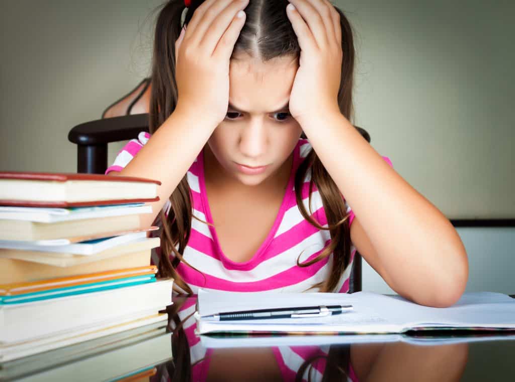 Angry and tired schoolgirl studying with a pile of books on her desk