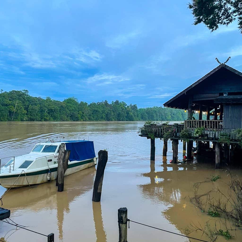 A Borneo rainforest lodge by the Kinabatangan river with a boat in the foreground