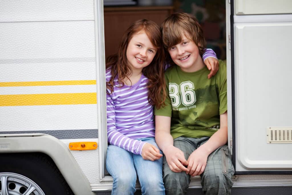 Two smiling children sitting in the doorway of a caravan 
