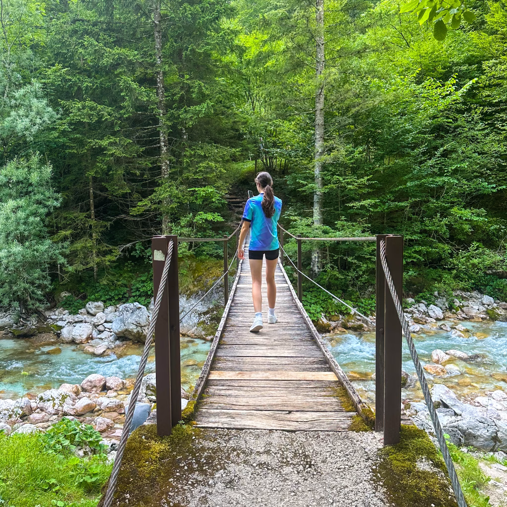 Girl walking over a small wooden bridge, blue coloured river and trees