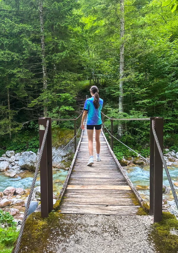 Girl crossing wooden bridge over blue river